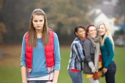 Girls who bully represented by a group of young girls looking on at one excluded girl while outside.